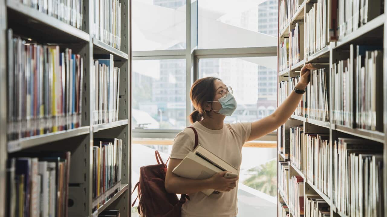 adult student wearing face mask looking at the books from the bookshelf