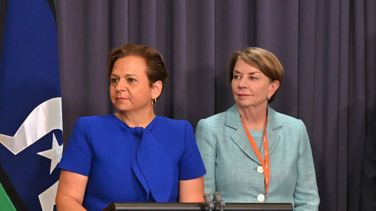 Two women with short hair wearing formal attire stand behind a black lectern