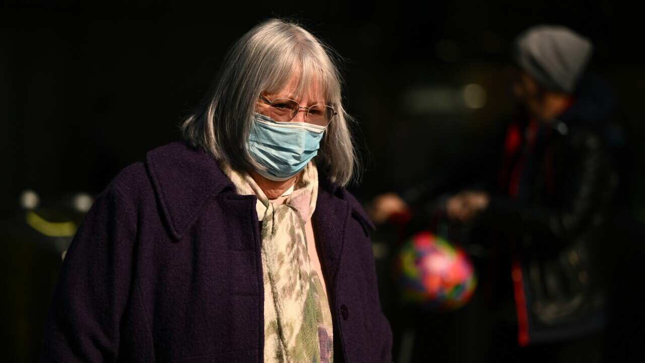 An older woman wearing a face mask walking through the street.
