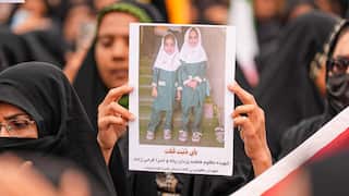 A woman standing in a crowd holds a photo of two young girls in school uniform