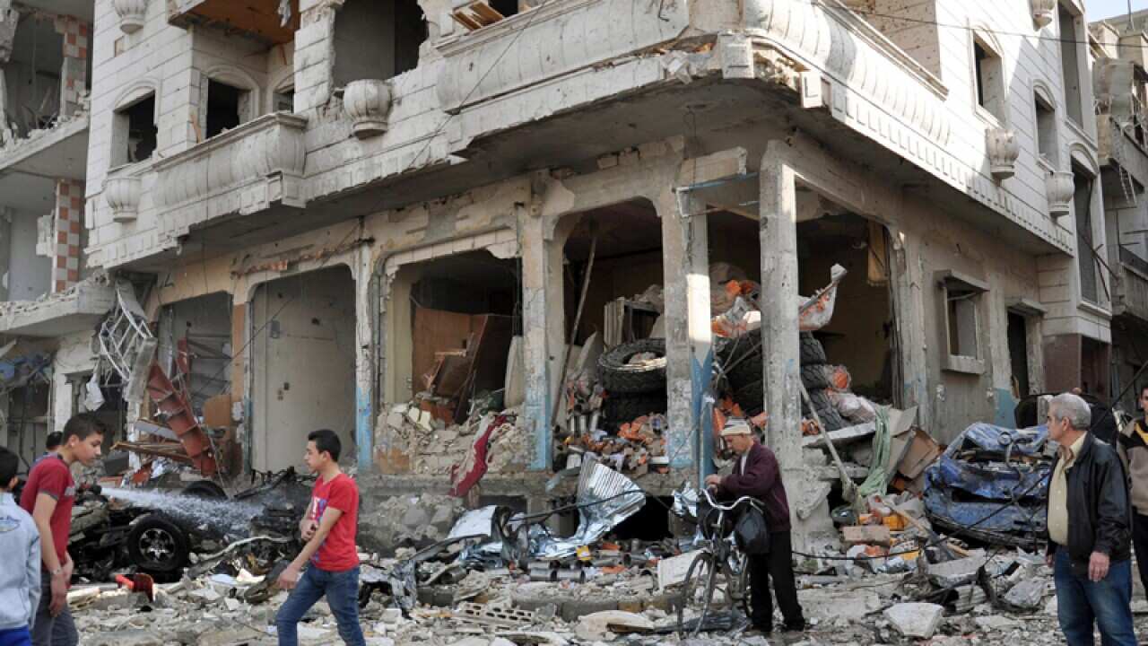 People walk by in front of damaged buildings in the city of Homs