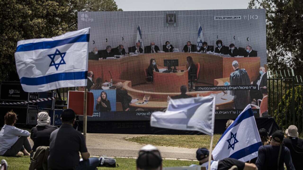 Israeli protesters hold national flags as they watch a live broadcast of the court proceedings