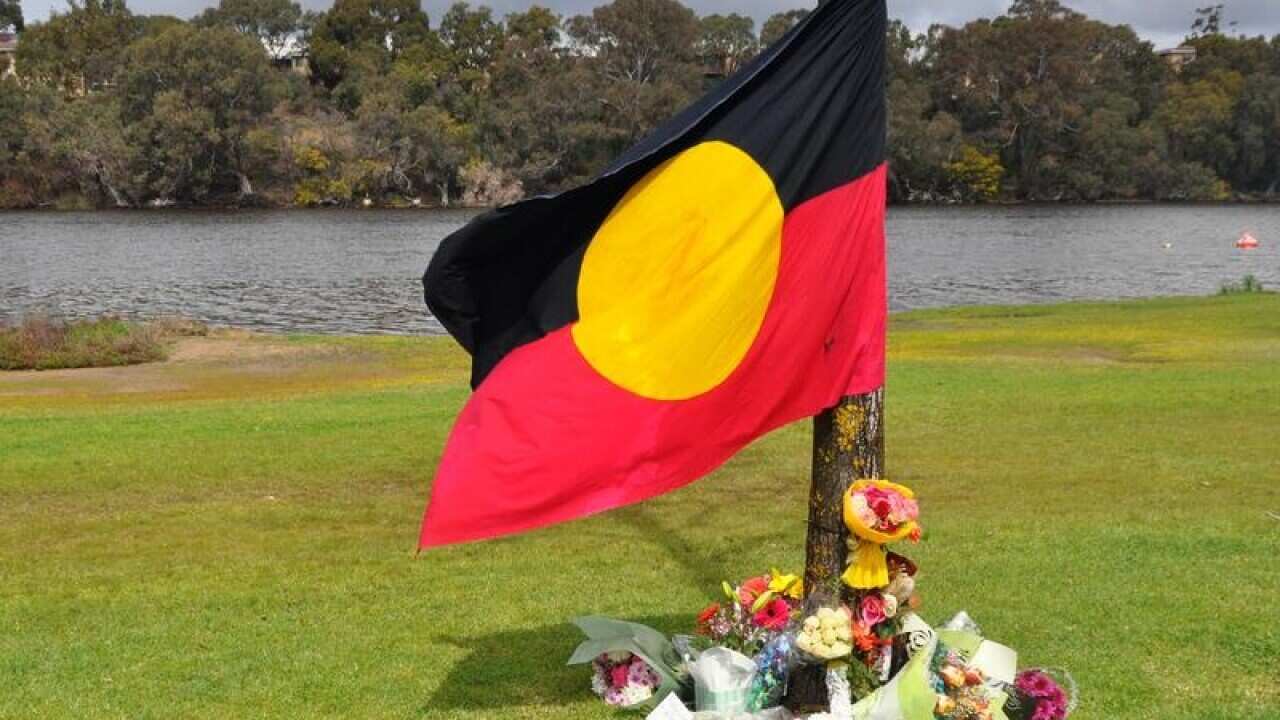 An Aboriginal flag is draped and floral tribute