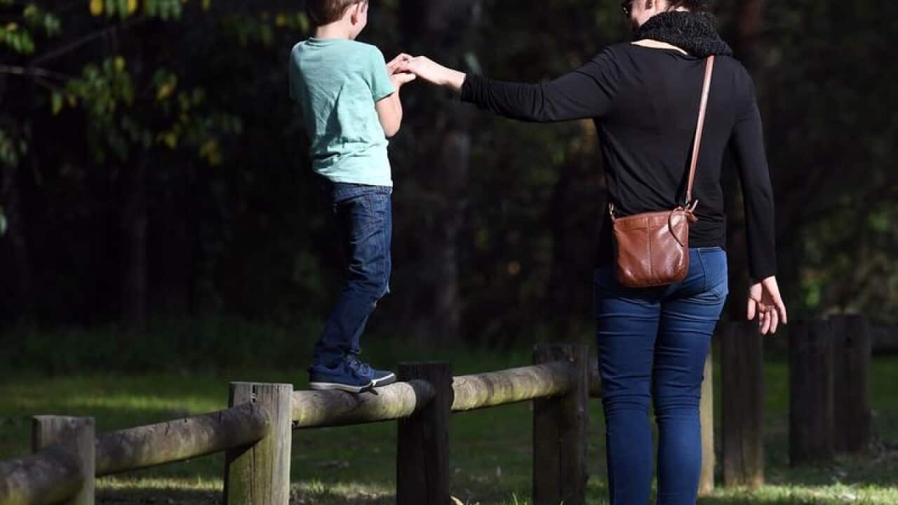 A young boy is assisted as he walks along a wooden pole.