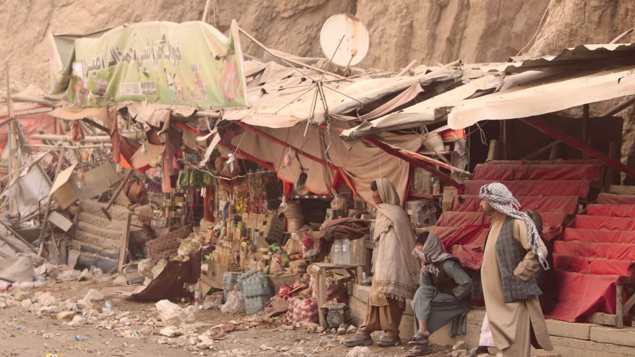 People sit along road lined with stalls and rubble