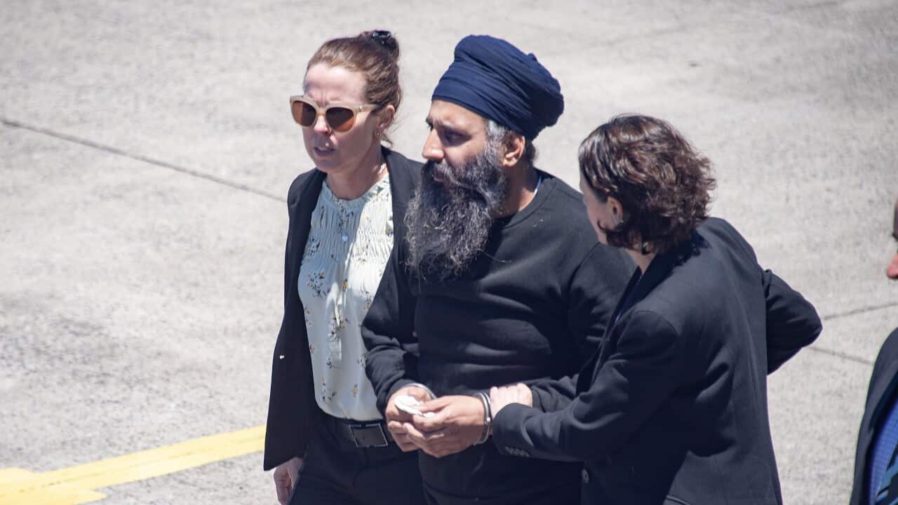 An Indian Sikh man in handcuffs is being escorted by two female police officers in civil clothes off a plane.