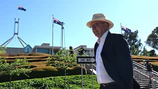 Prime Minister Anthony Albanese in a suit and white shirt, wearing a sun hat as he walks into work, with parliament and Australian flags in the background.