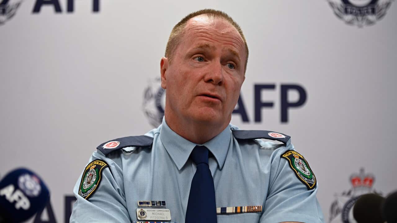 A man wearing a police uniform speaking while seated in front of microphones.
