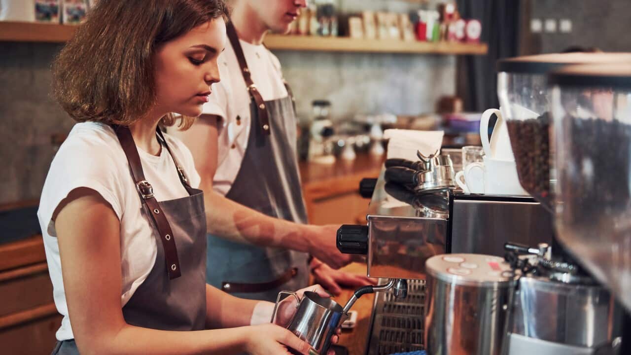 Two teenagers operating an espresso machine.