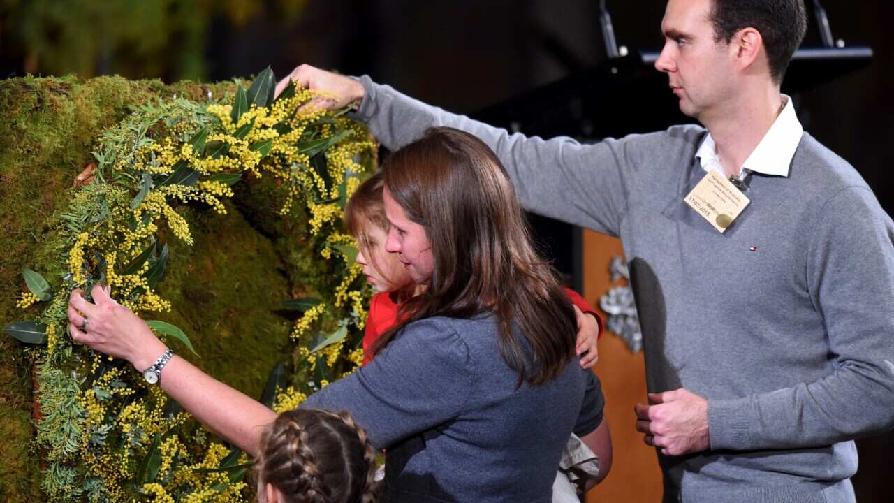 Family members of a victim place a wattle sprig at a wreath during a national memorial service to honour the people that died as a result of the downing of Malaysian Airlines Flight 17 at Parliament House in Canberra