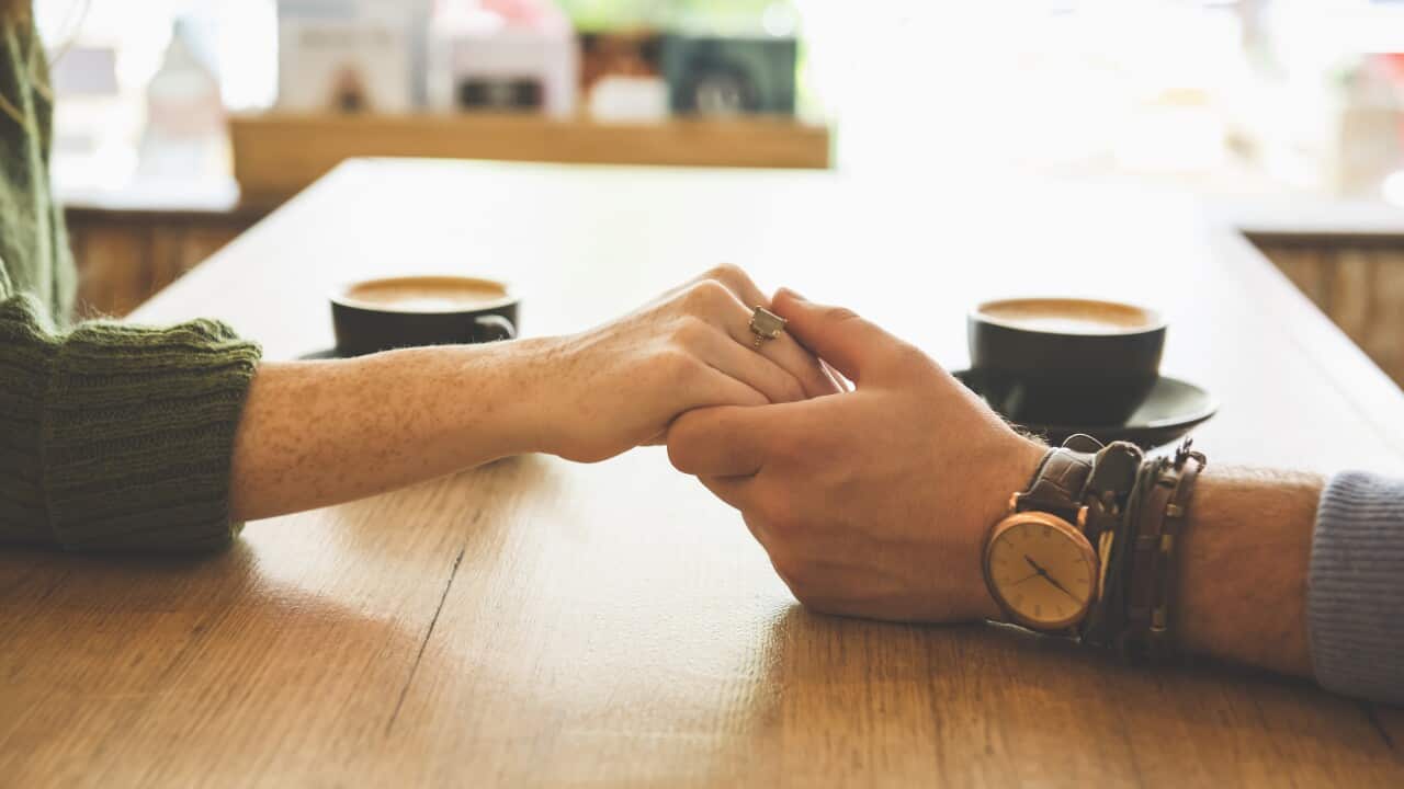 Close up of Caucasian couple holding hands in coffee shop.
