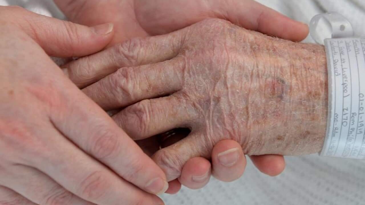A nurse holds the hand of an elderly patient