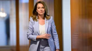 A woman in a pale blue suit walks down a wooden hallway