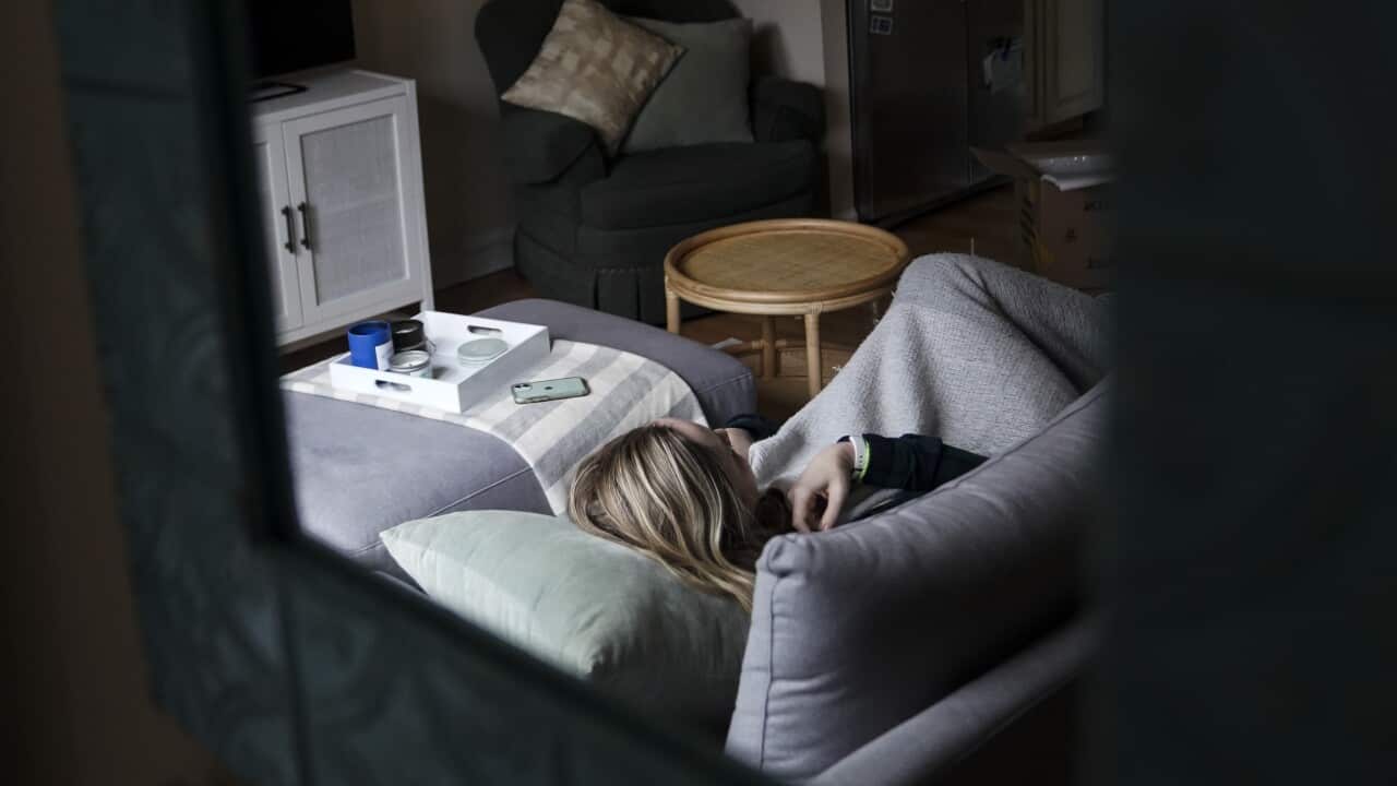 A woman with blonde hair lying down on the couch wrapped in blankets.