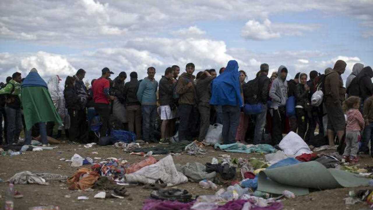 In this file photo, migrants and refugees queue as they wait for a police bus to take them to a detention center close to Hungary's border 