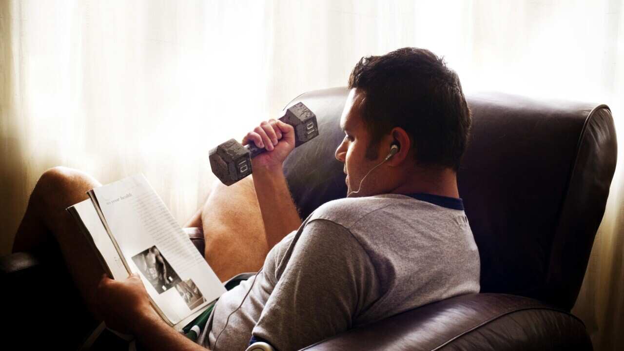 Man reading magazine while working out with dumbbells.