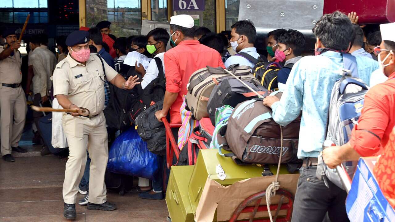 Police personnel instructs the migrants to stand in a queue as they arrive to board the train