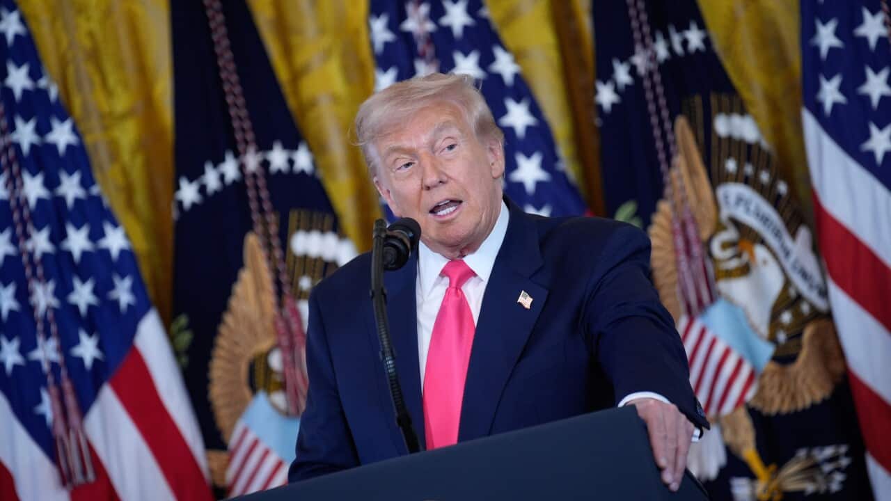 Donald Trump speaking at a podium. Behind him are flags.