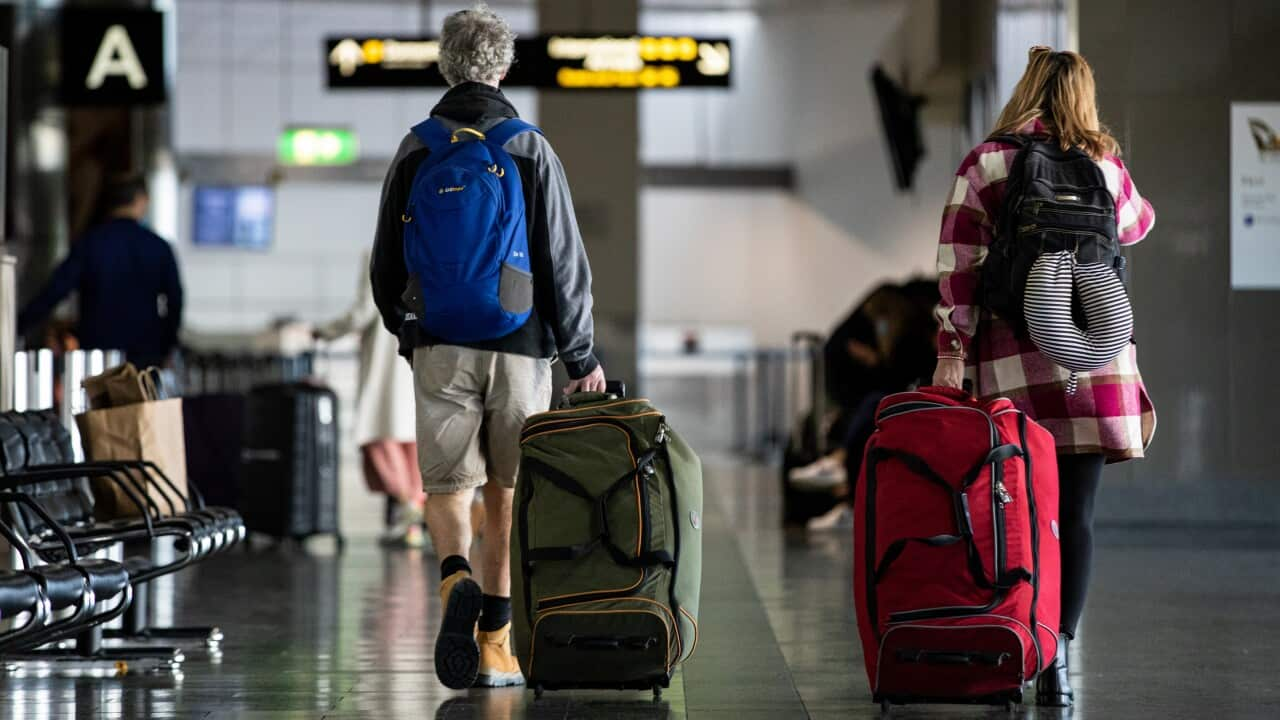 Two people wheeling their suitcases through the departures hall at an airport.