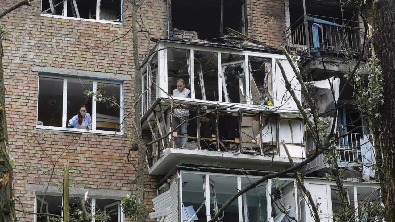 Residents clear debris at a residential building with shattered windows and fire damage.