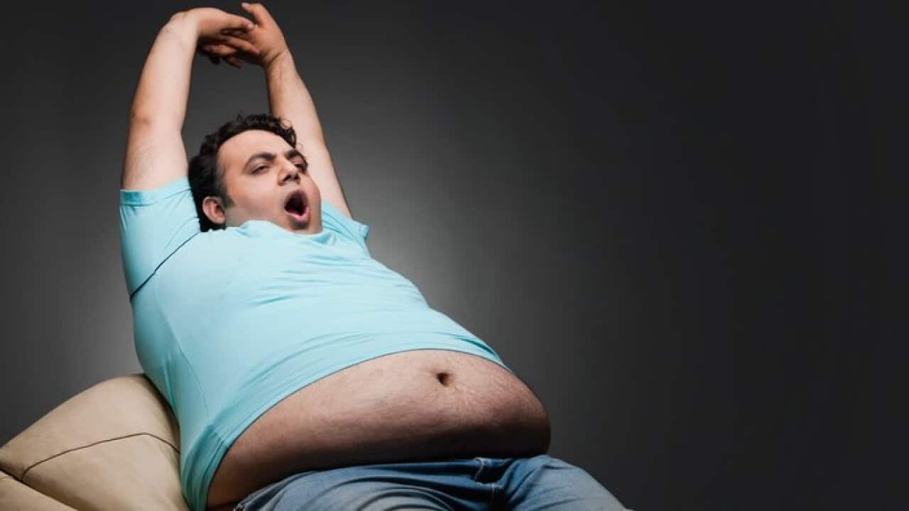 Overweight man sitting in bean bag, stretching and yawning, studio shot