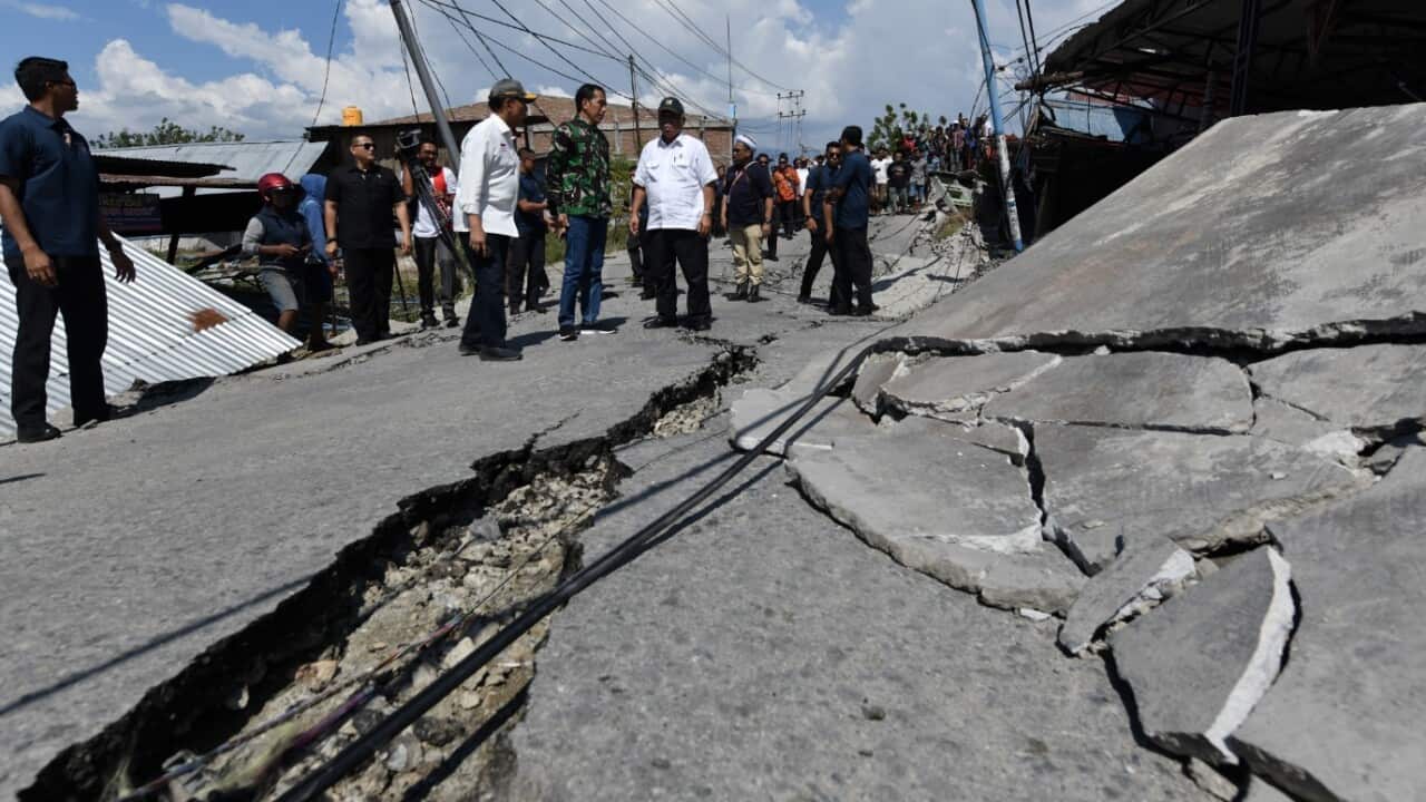 A handout photo made available by the Indonesian Presidential Palace showing Indonesian President Joko Widodo (C) looking at a ruined house
