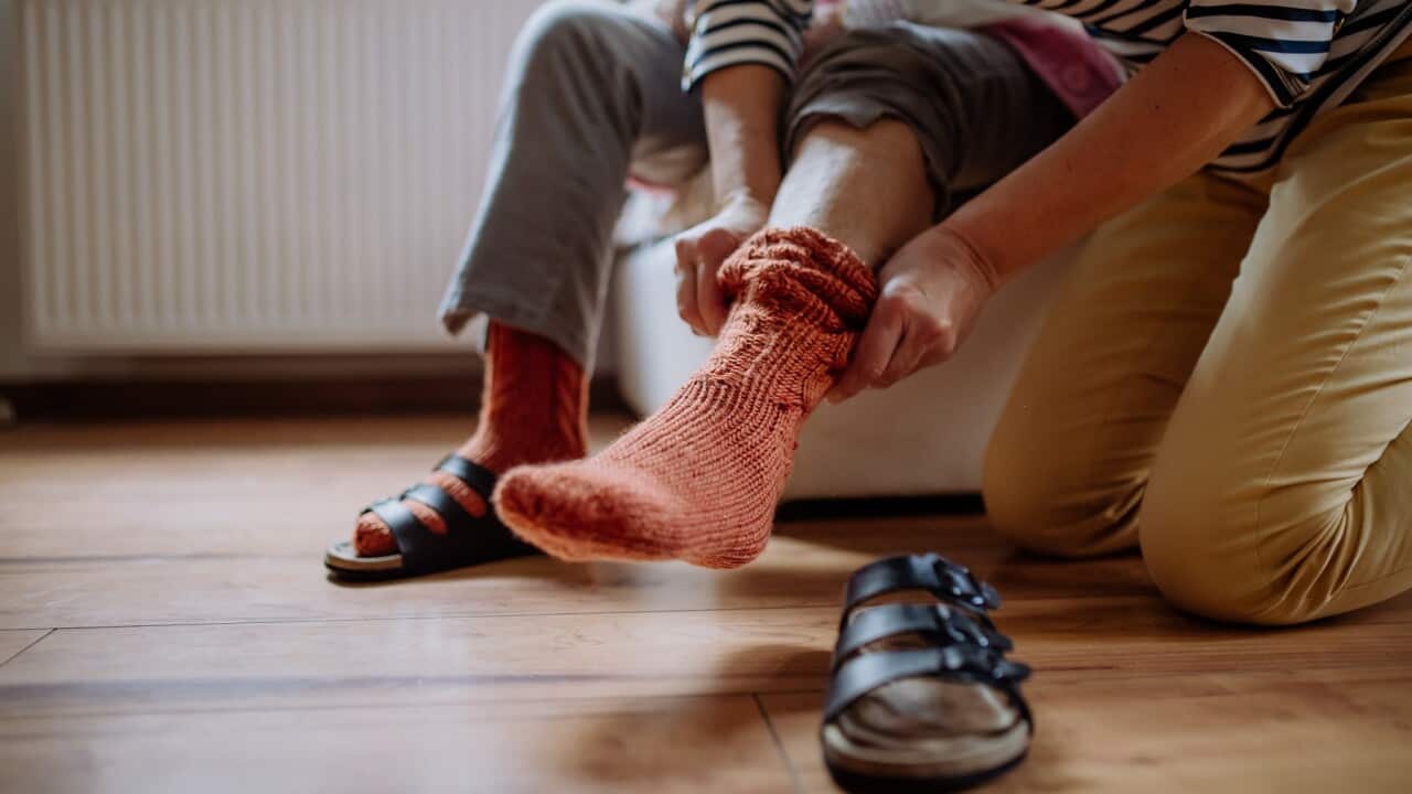 Close-up of healthcare worker putting on warm socks to senior woman.