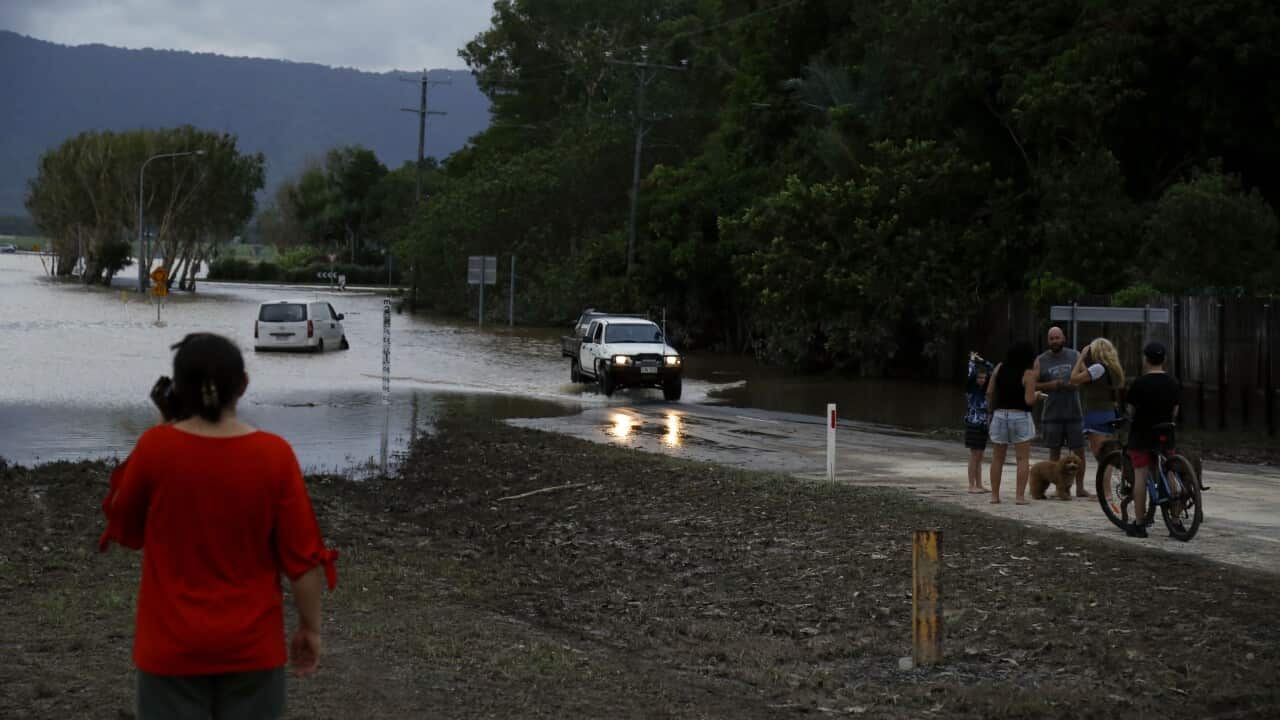 A car drives through floodwater as several people look on
