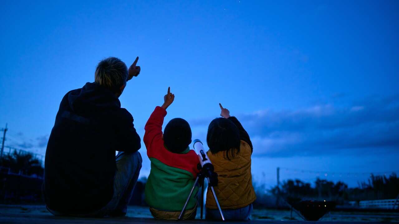 Silhouette of father and son pointing to sky.