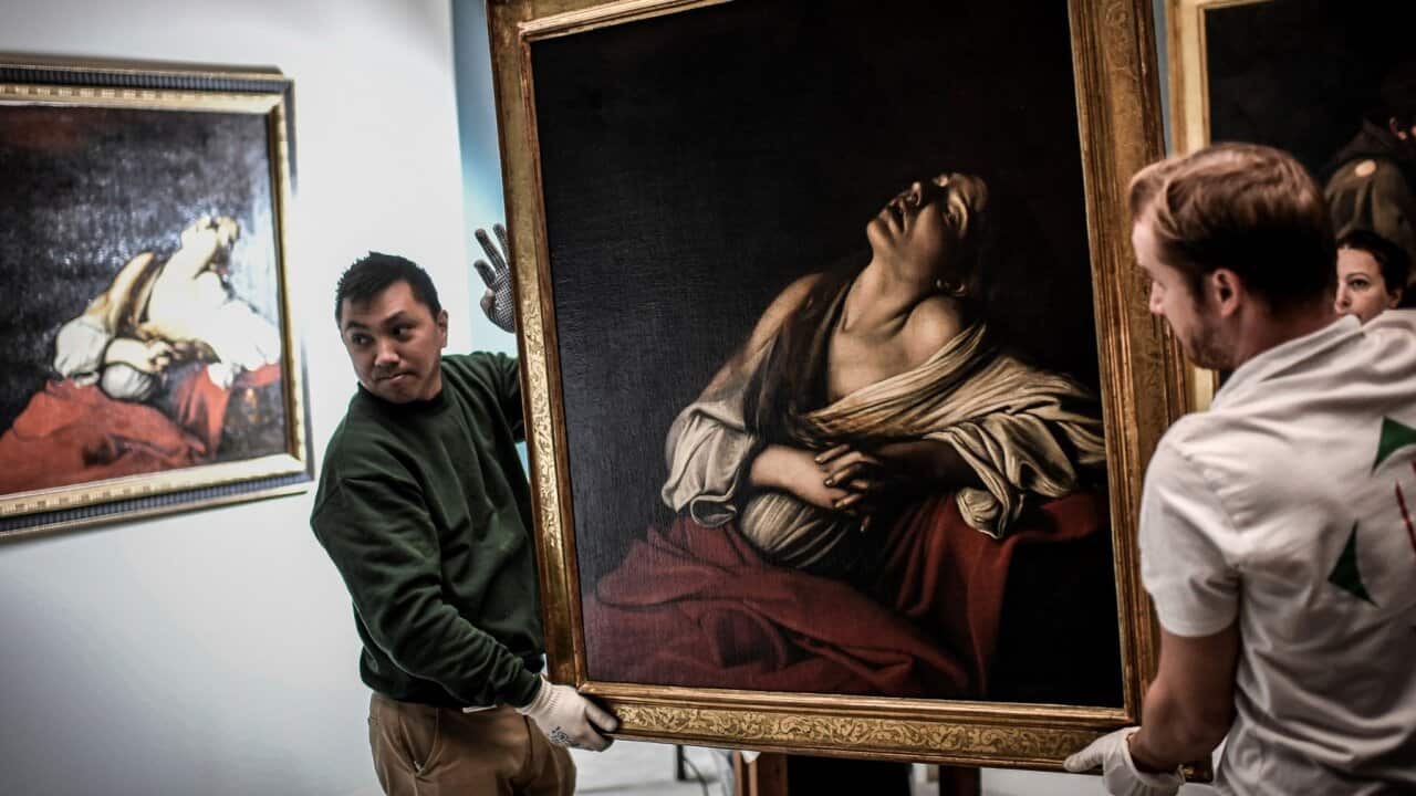 Employees carry a painting called "Mary Magdalen in Ecstasy" and created by Italian painter Caravaggio, as they walk past a second painting with the same title.