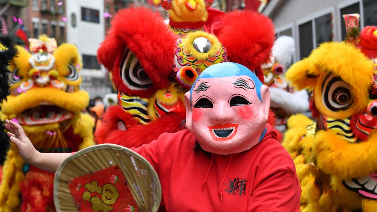 A person wearing a mask dances as people in dragon costumes dance behind them.