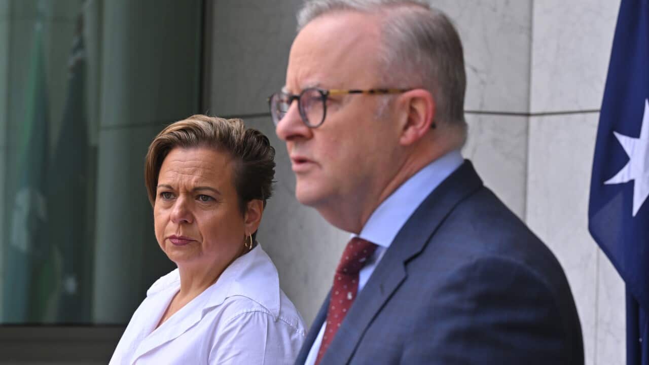 A woman in a white shirt with short hair stands next to a man in a dark suit