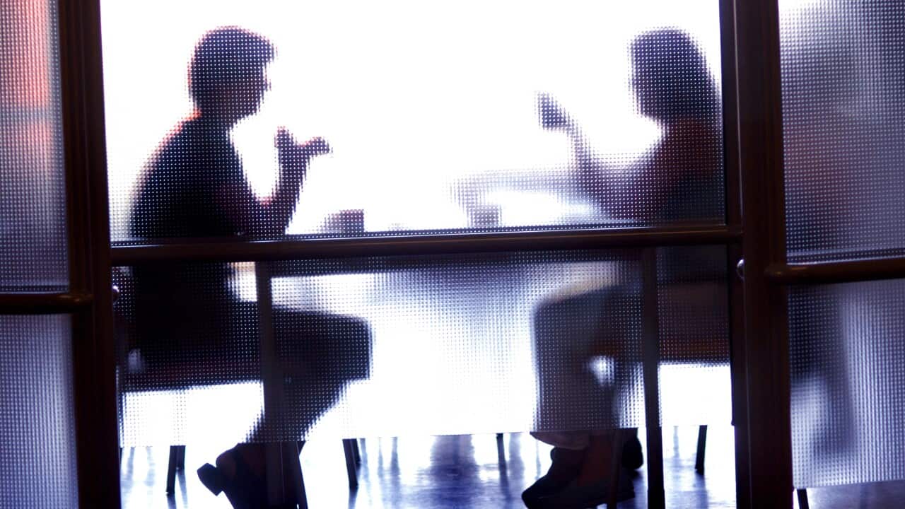 Two people's silhouettes behind a glass door. They're seated at a table talking.