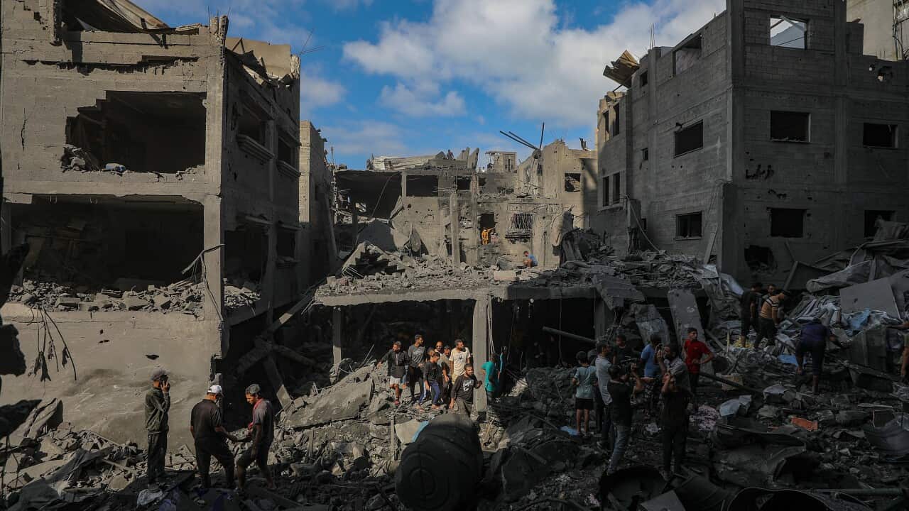 People stand amid the rubble and wreckage of heavily damaged buildings.