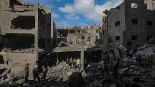 People stand amid the rubble and wreckage of heavily damaged buildings.