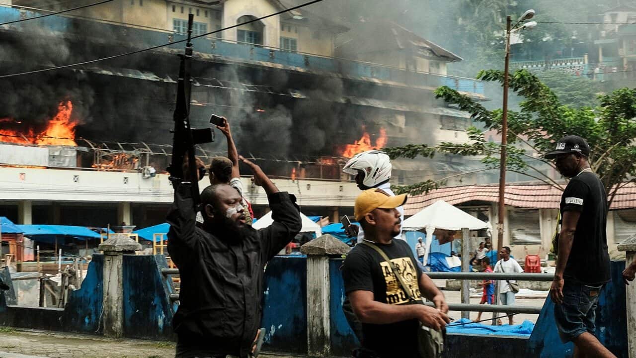 A Papuan police officer carries a riffle as he controls the crowd after protesters torched Buruni market during a violent protest in Fakfak, West Papua.