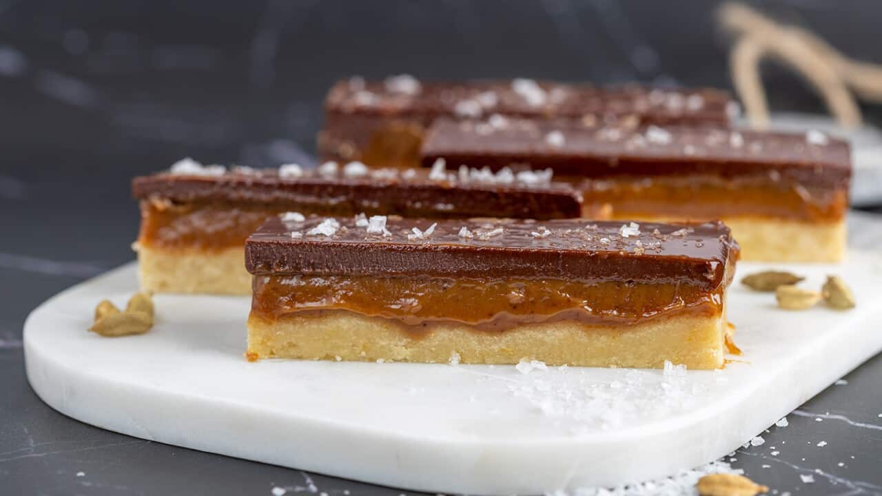 Four fingers of a rich slice sit on a white platter. The bars have three layers - a shortbread base, a gooey-looking caramel middle and a top later of chocolate, which is dusted with salt flakes.