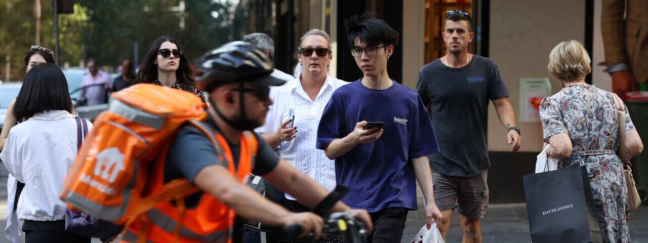 People crossing a road as a cyclist rides past.
