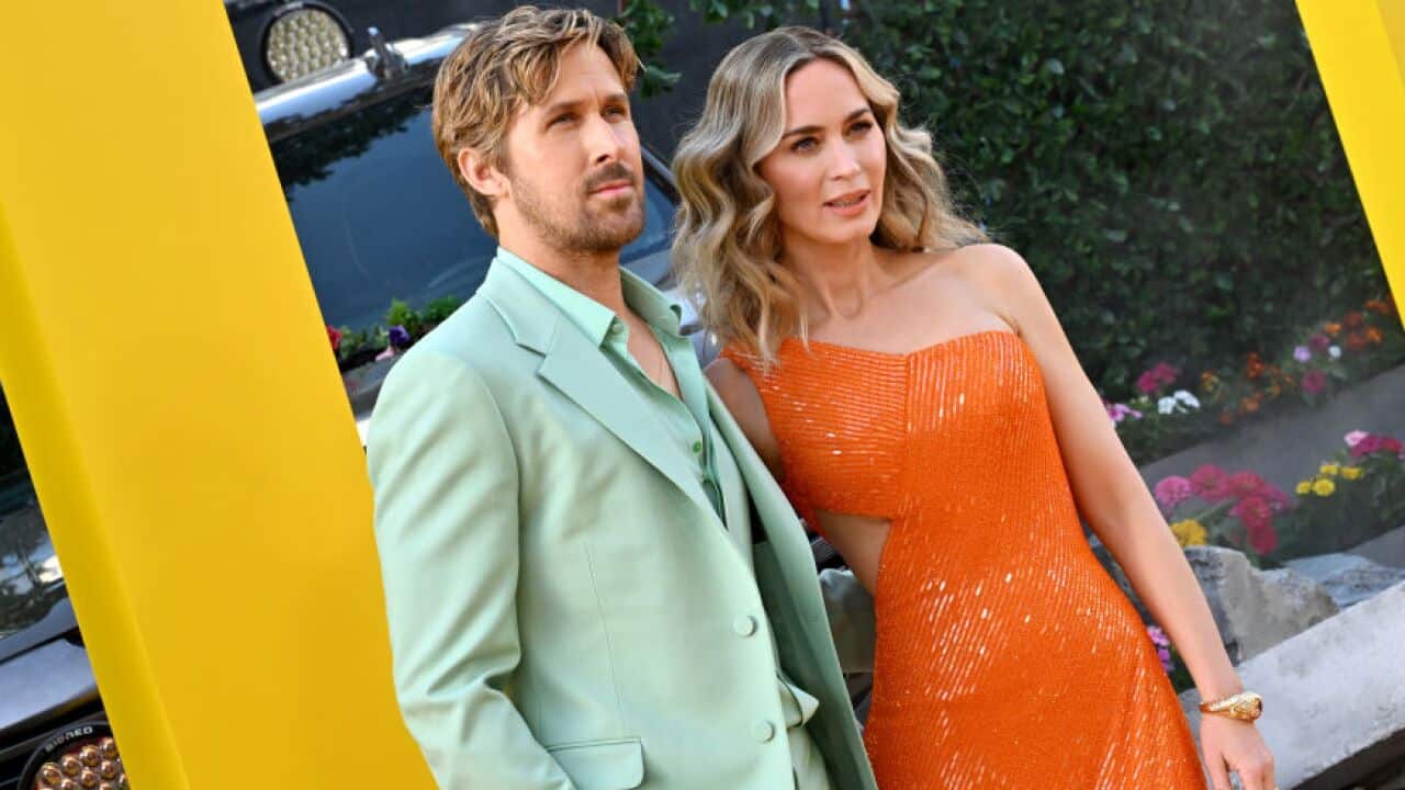 Ryan Gosling wearing a pale green suit standing net to Emily Blunt, wearing an orange dress