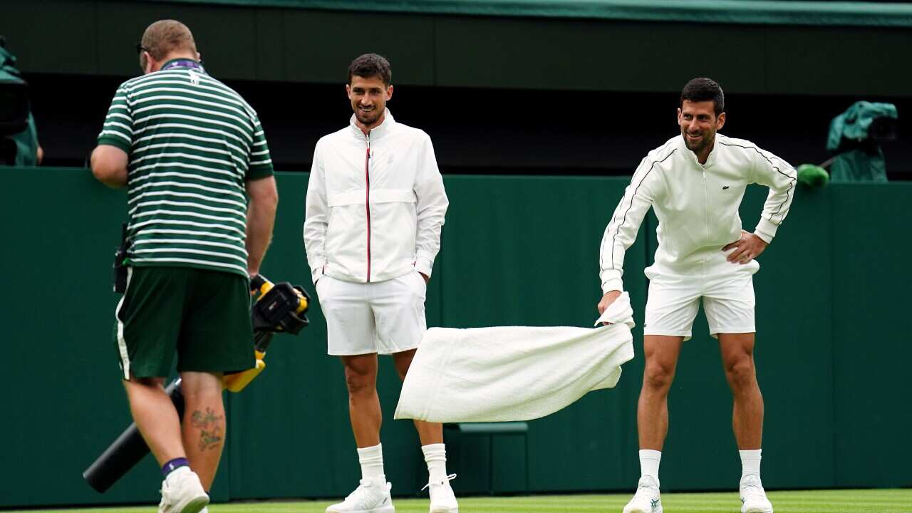 Novak Djokovic of Serbia and Argentinian Pedro Cachin inspect the moisture on court and watch the ground staff drying grass