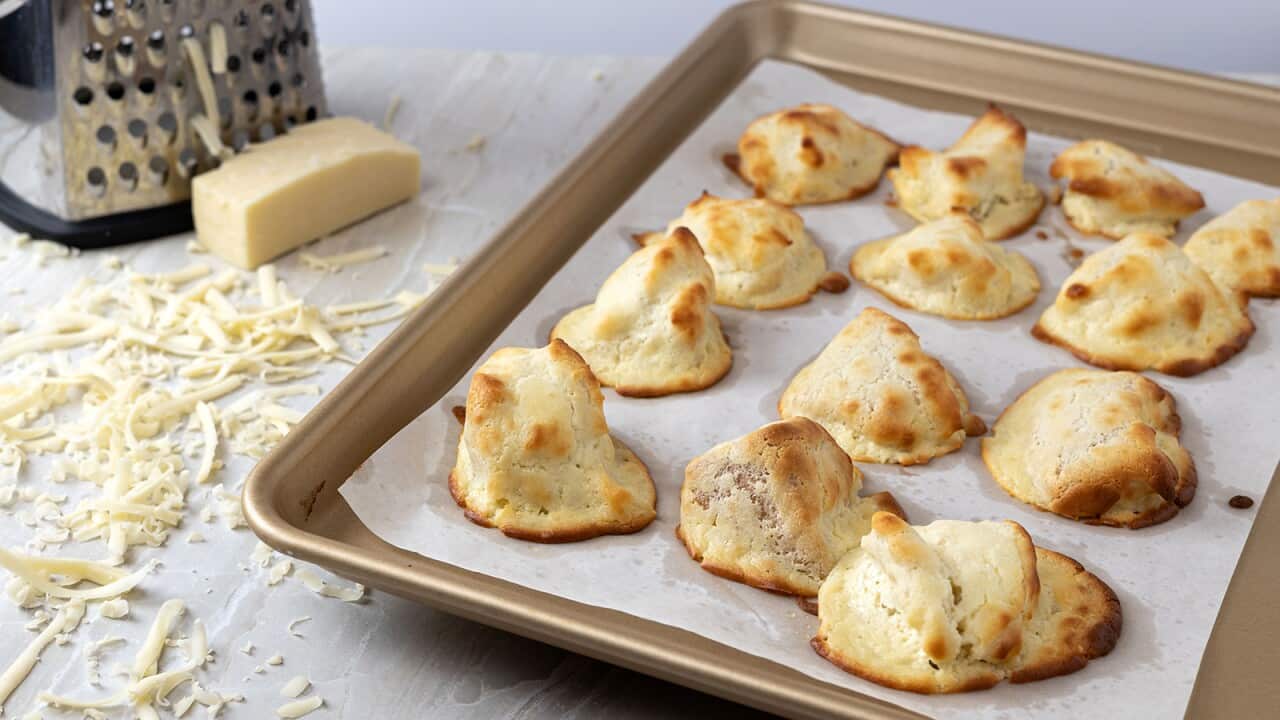 12 roughly conical pale yellow puffs with golden brown edges sit on a baking sheet.