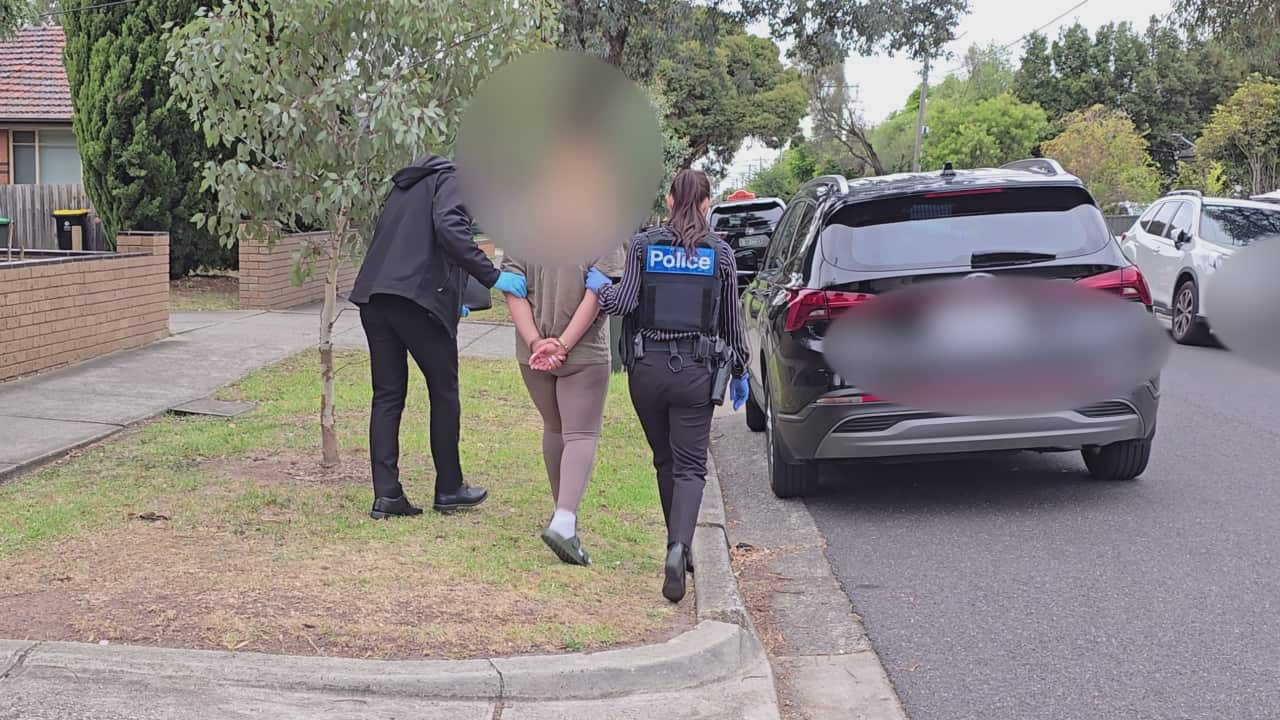 Two police officers escort a handcuffed woman to a parked police vehicle.
