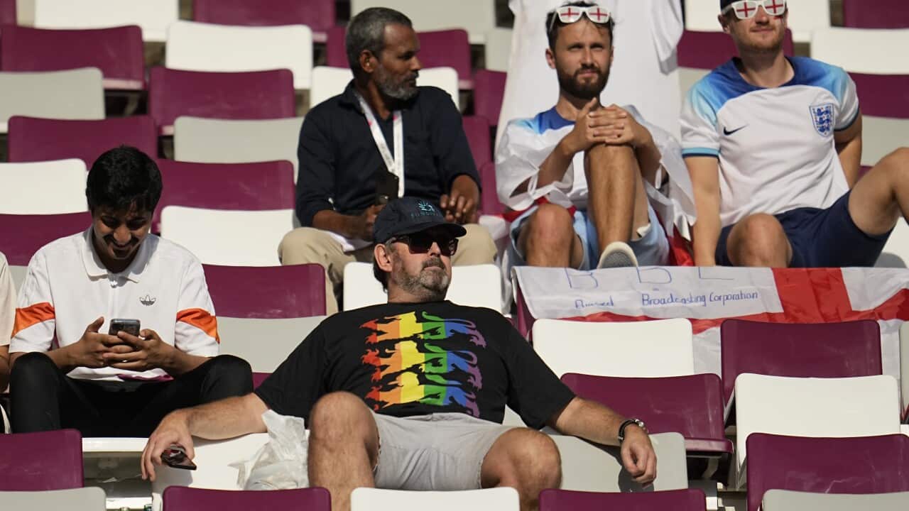 A man wearing a rainbow football top seated in a stadium.