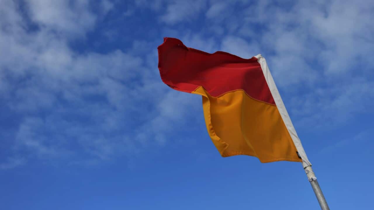 A lifeguard on duty flag stands in the sand