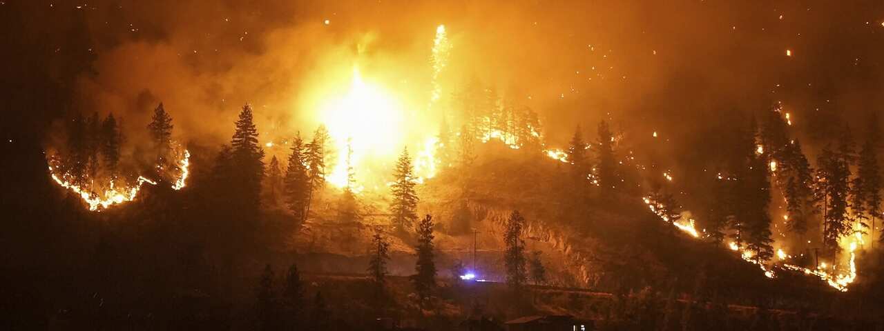 The McDougall Creek wildfire burns on the mountainside above a lakefront home in West Kelowna, lighting up the night time sky.