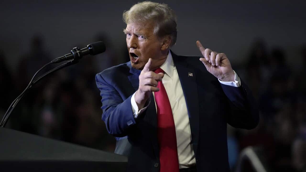 A man wearing a suit and tie speaking while standing in front of a microphone.