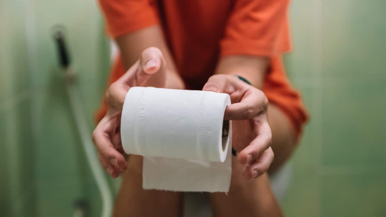 Woman sitting on toilet holding toilet paper roll