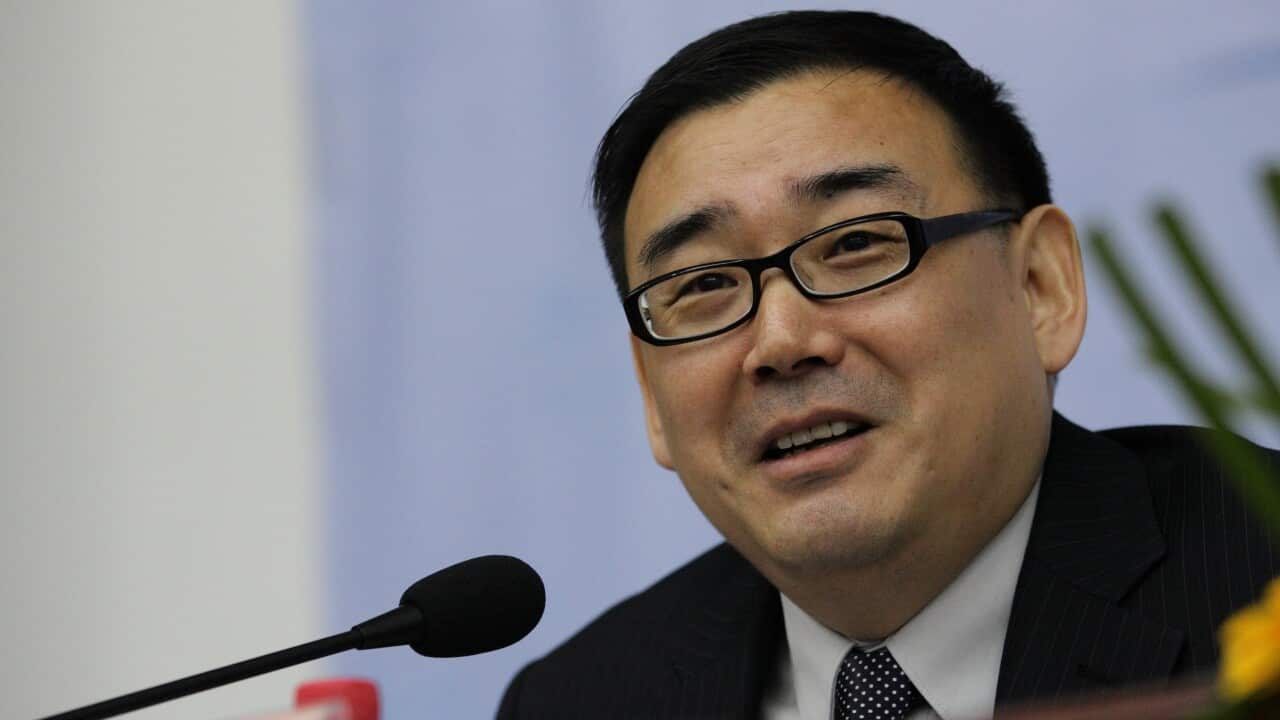 A man wearing glasses and a black suit speaks into a lectern microphone