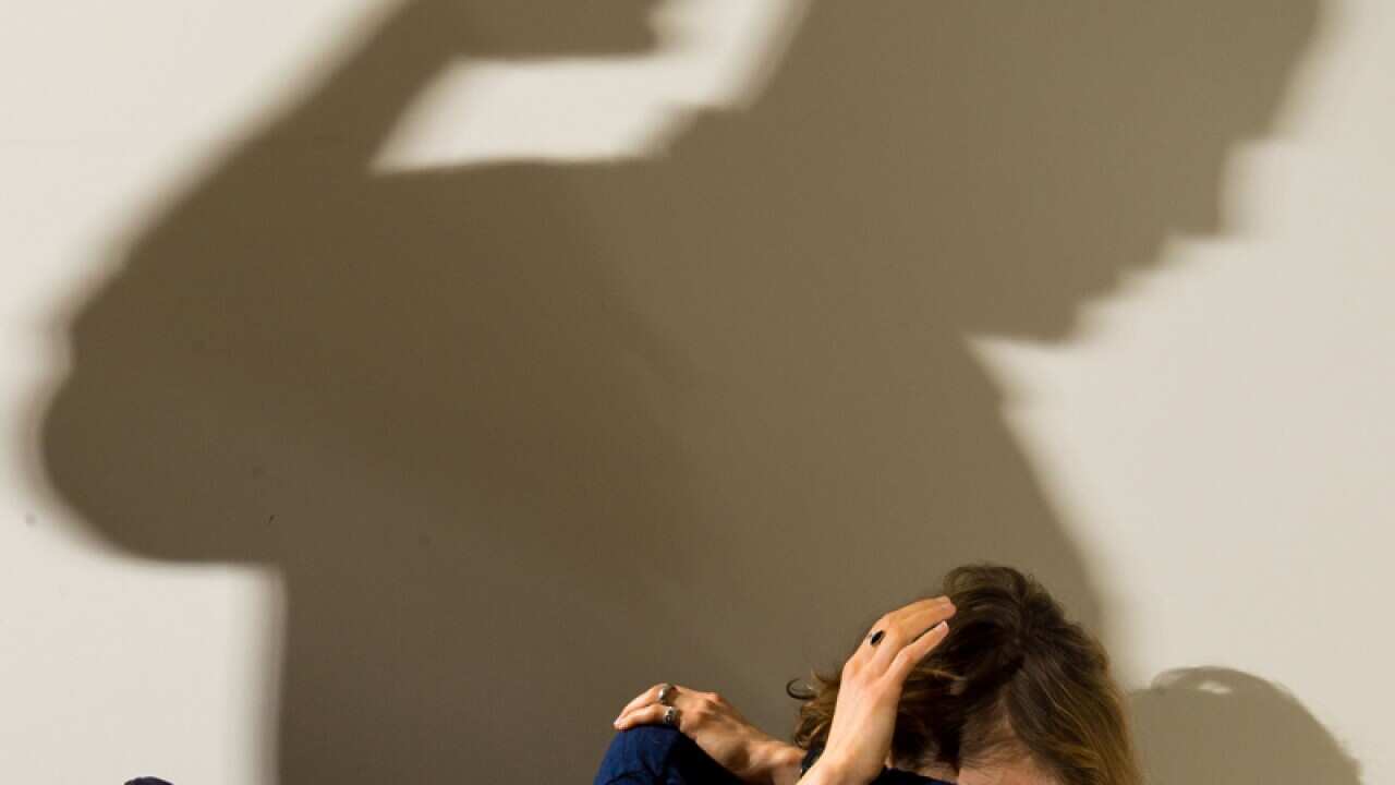 A shadow of a man with a clenched fist as a woman cowers in the corner