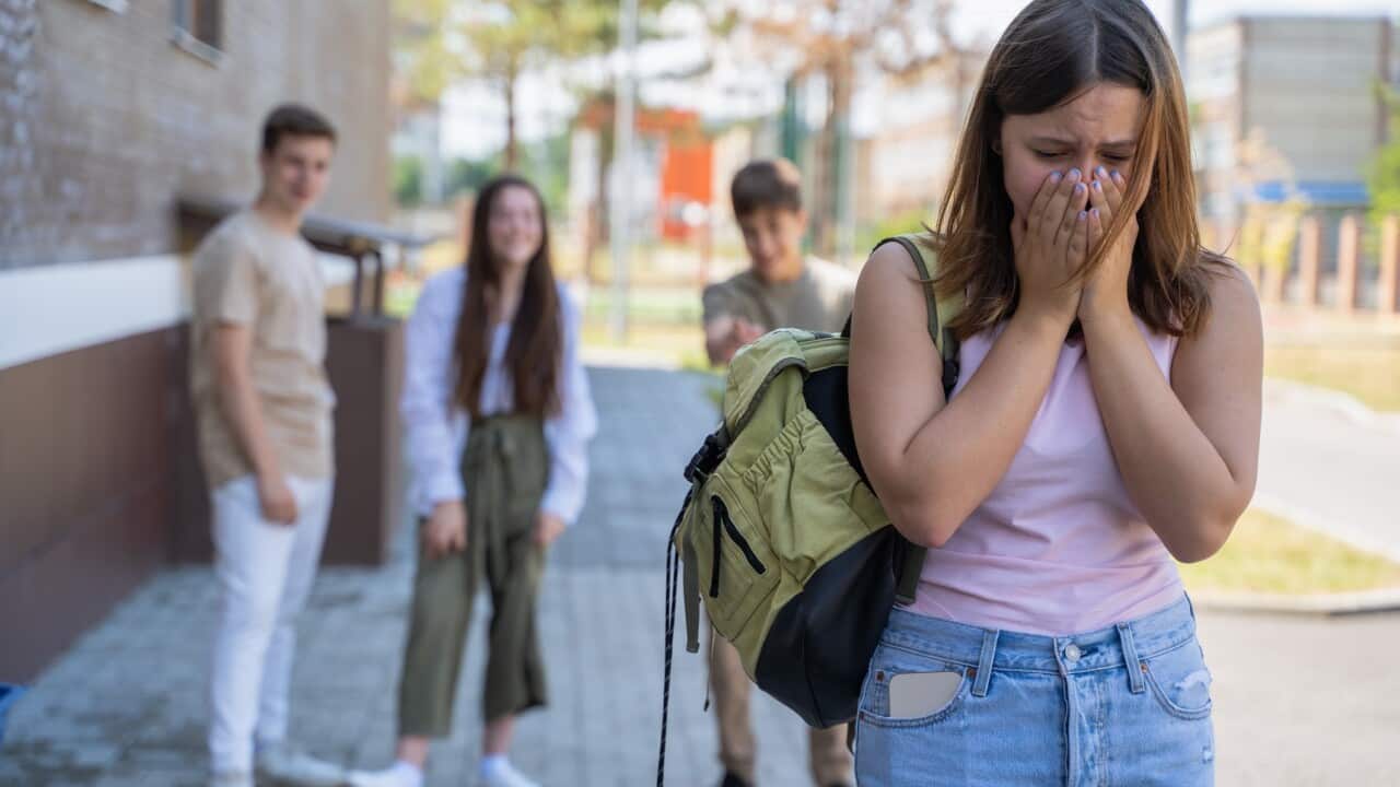 School bullying. Crying girl with laughing teenagers behind her at school yard